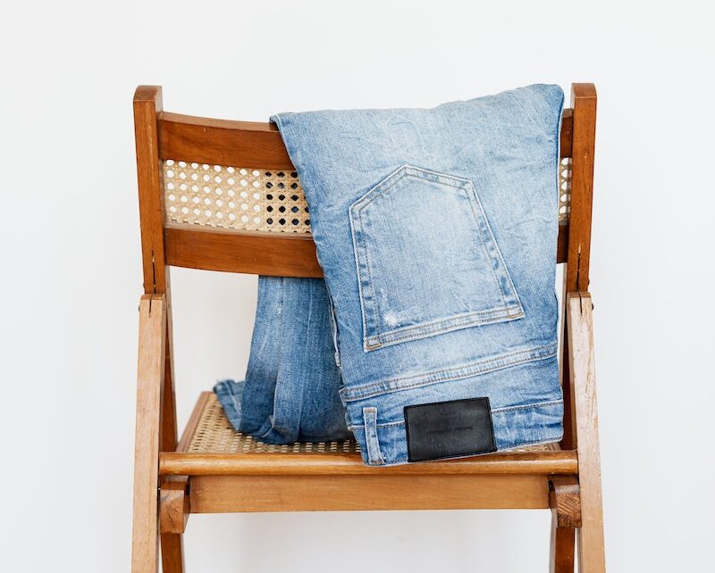 Trendy blue jeans put on back of wooden chair near empty white wall