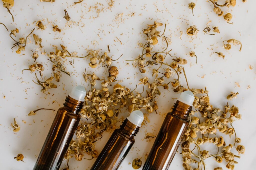 Bottles of Oil with Rollers and Dried Flowers on a White Surface