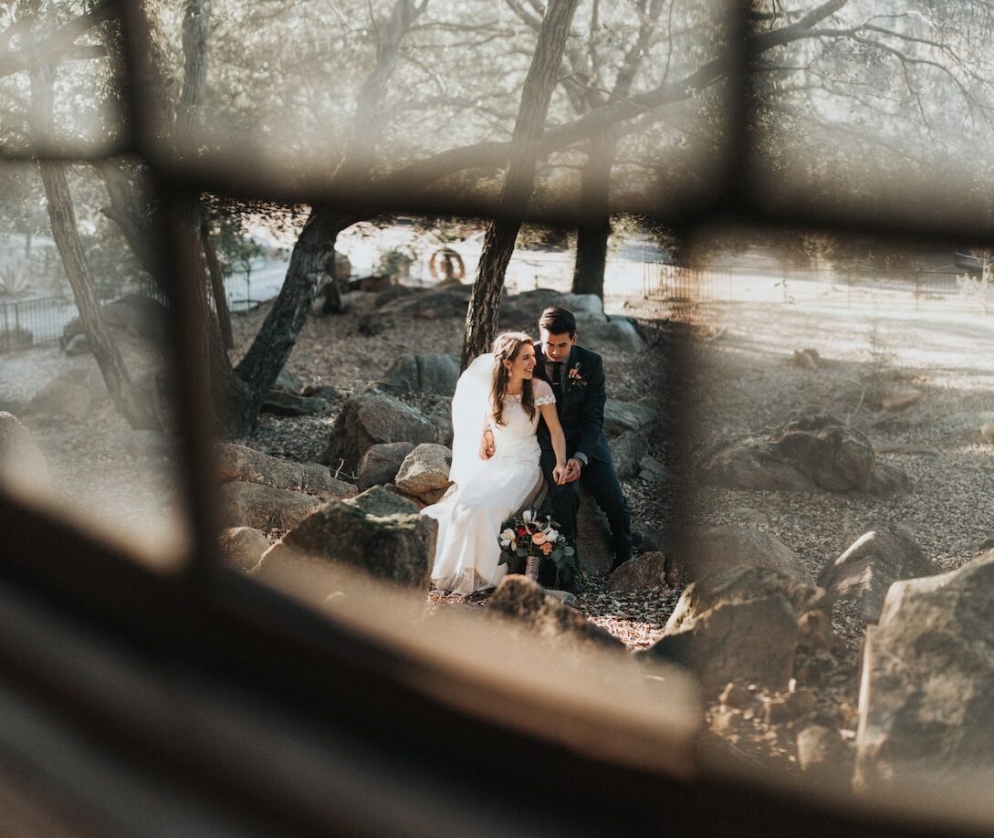 bride and groom sitting on rock holding hands