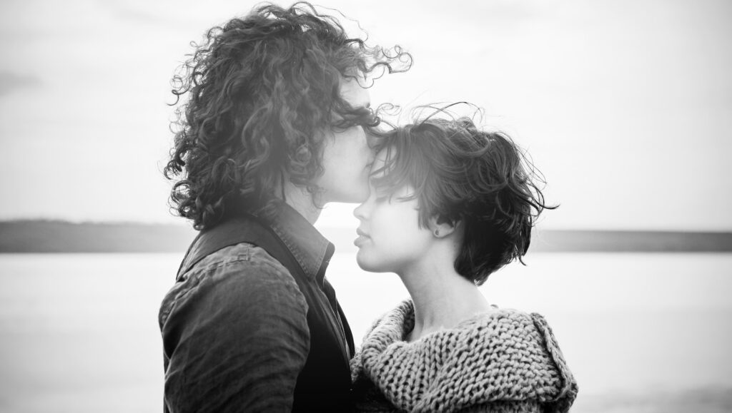 grayscale of man kissing woman's forehead