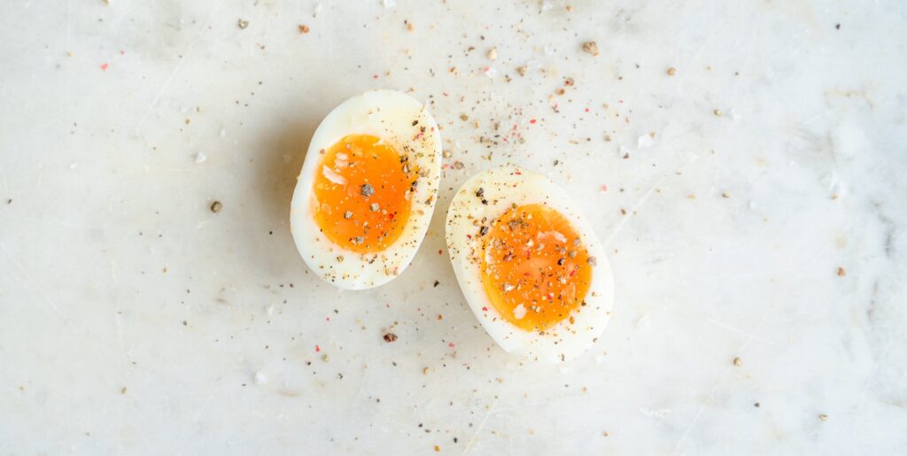 Top view of halved soft boiled egg placed on marble table and spiced with salt and pepper