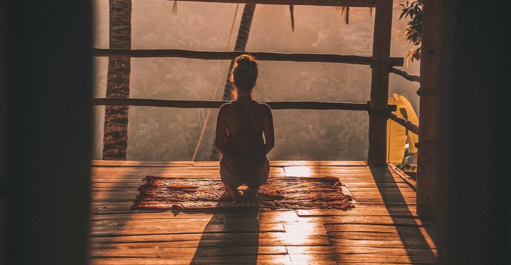 woman meditating on floor with overlooking view of trees