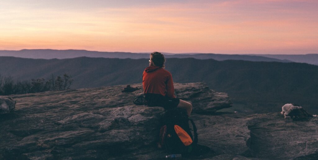 person sitting on boulder overlooking mountain during golden hour