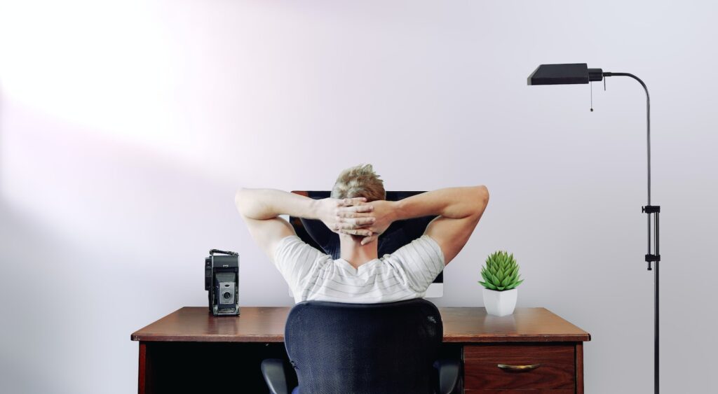 man holding his head while sitting on chair near computer desk