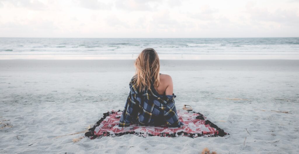 woman sitting on blanket located on shoreline