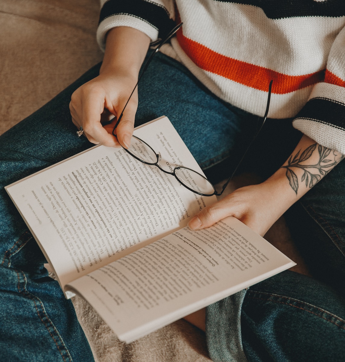 person reading book while holding eyeglasses