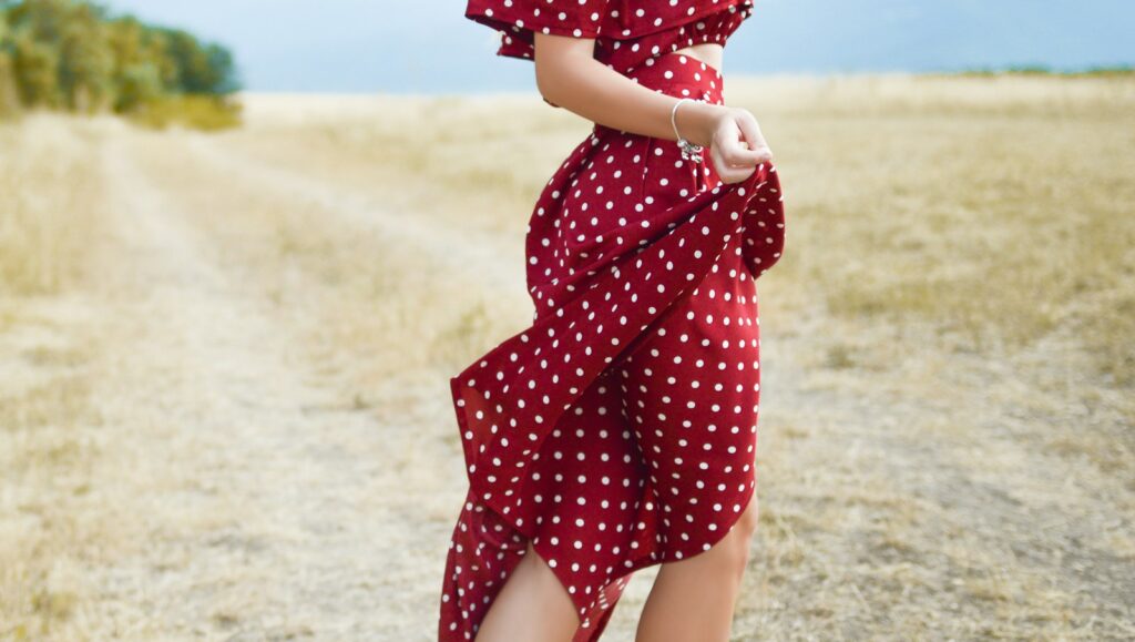 woman in red polka-dot dress standing in the middle of grass field during daytime