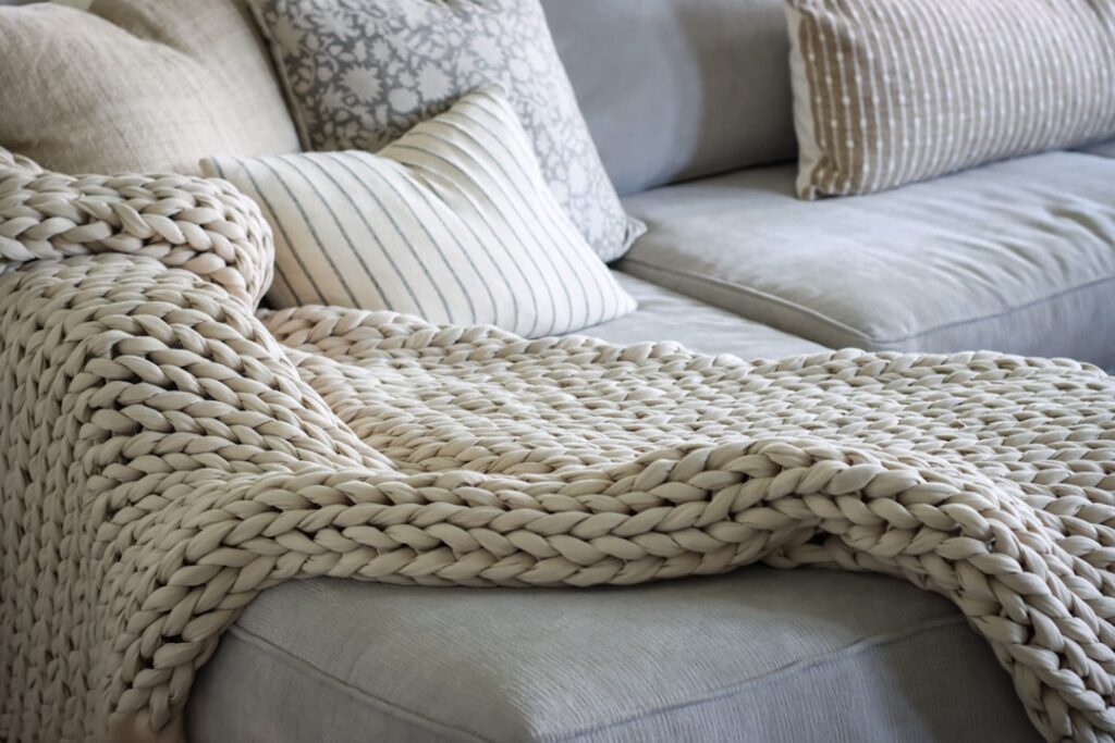 Cream chunky knit throw draped over a beige sofa with green cushion and potted plant