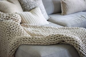 Cream chunky knit throw draped over a beige sofa with green cushion and potted plant